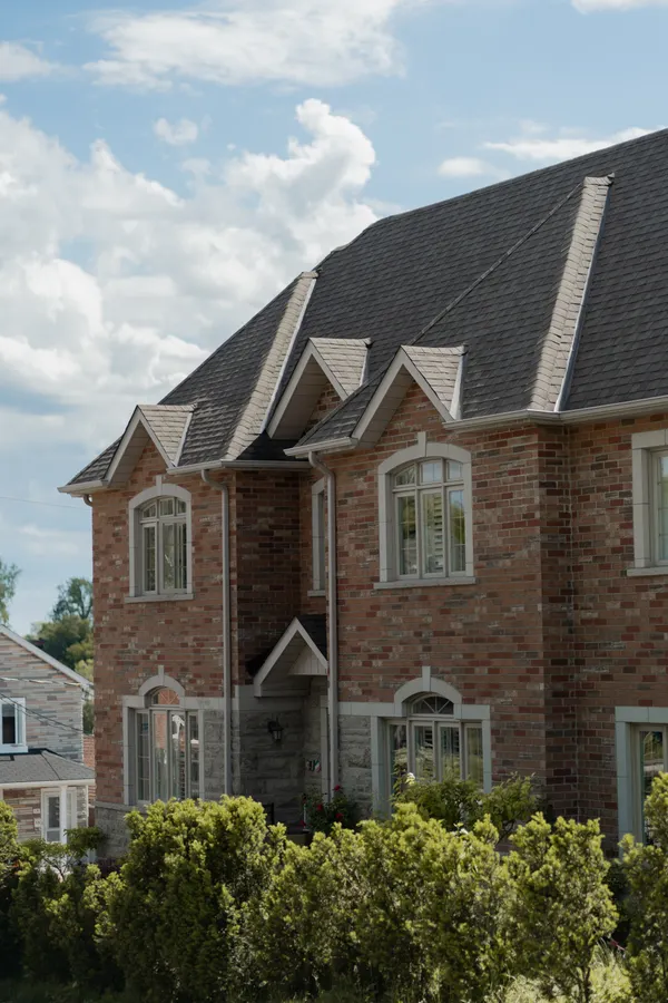 A brick home with dormers and a steep shingled roof under a bright sky.