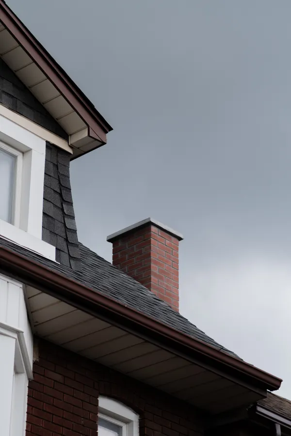 Dark shingles running up to a brick chimney under an overcast sky.