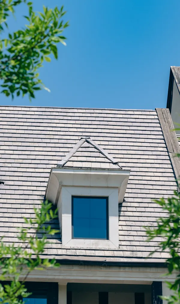 A dormer window and roof edge against a blue sky, the gutter line running clean along the eave.