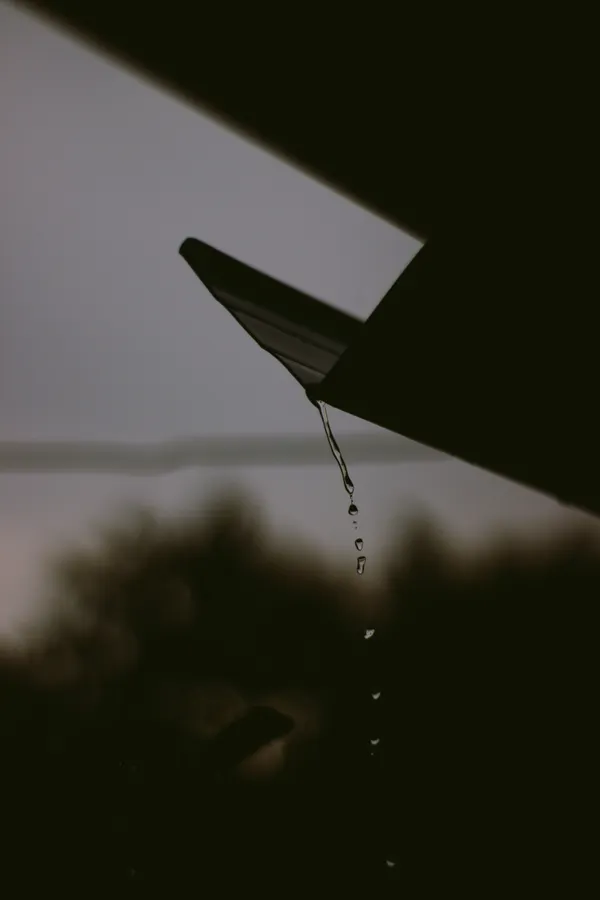 The mouth of a downspout at the end of a run, dripping after rain.