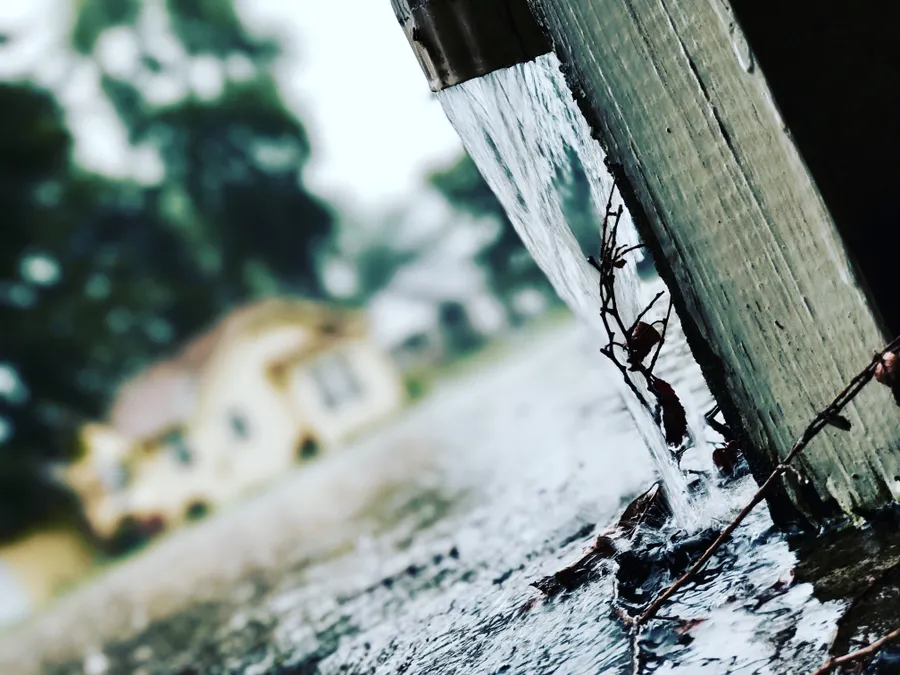 Water pouring from a downspout onto the ground beside a house after heavy rain.
