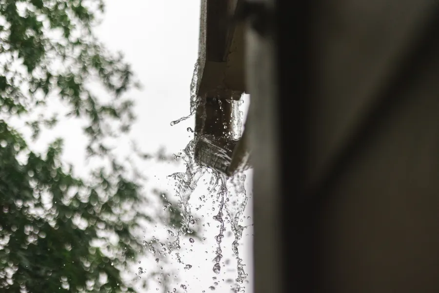 Water spilling over the front edge of a blocked gutter.