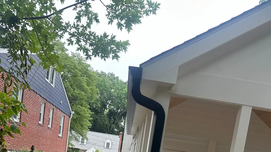A finished black gutter and downspout on a newly built white porch, water directed out onto a fresh mulch bed.